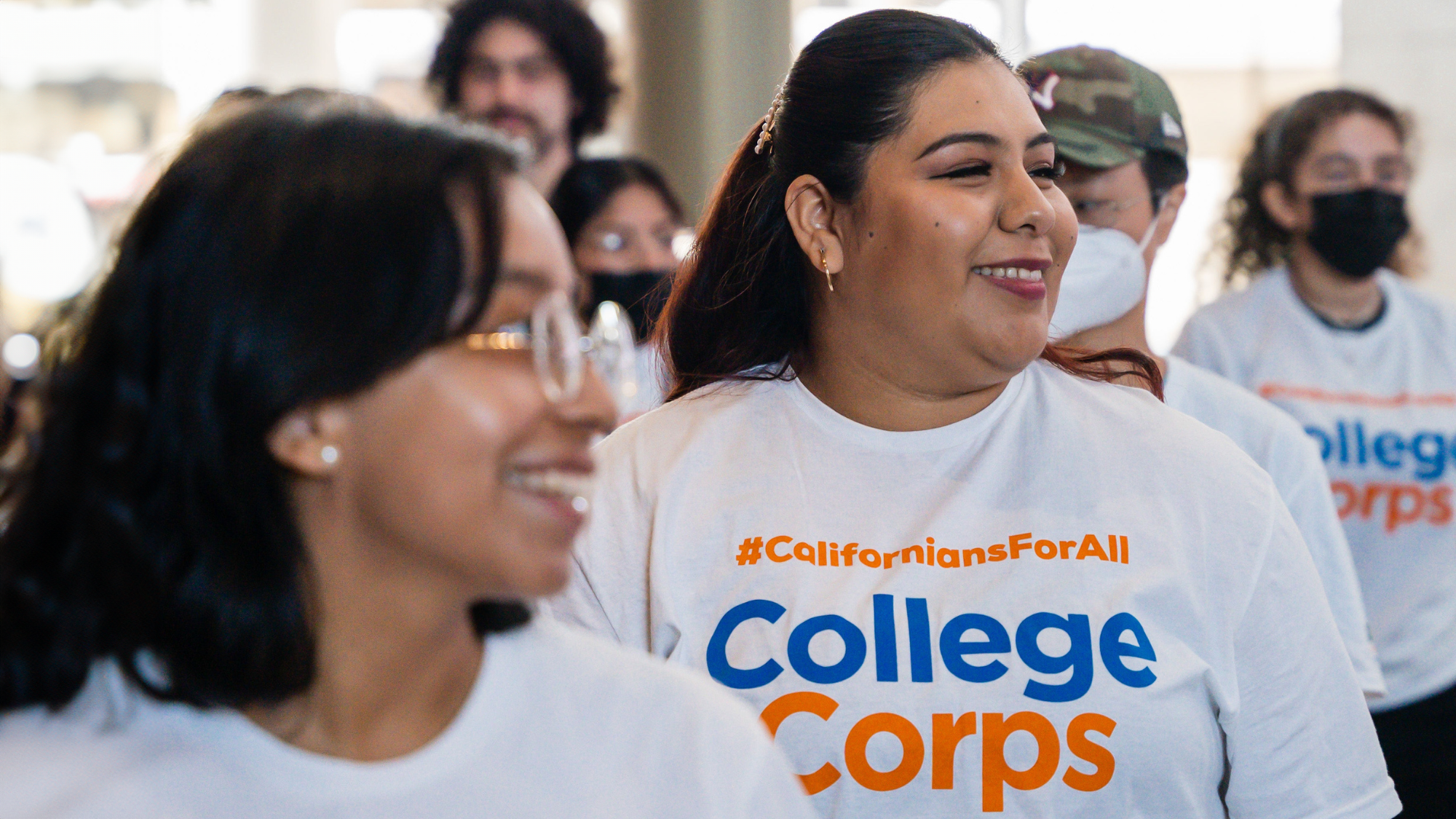 Close up of a student smiling among a group. Student wears a shirt with the text "#CaliforniansForAll"